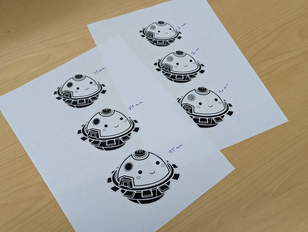 Two black and white printouts on a wooden background. On each printout, three cartoon representations of the DAVINCI probe in different sizes. Measurements have been hand-written next to each cartoon print.